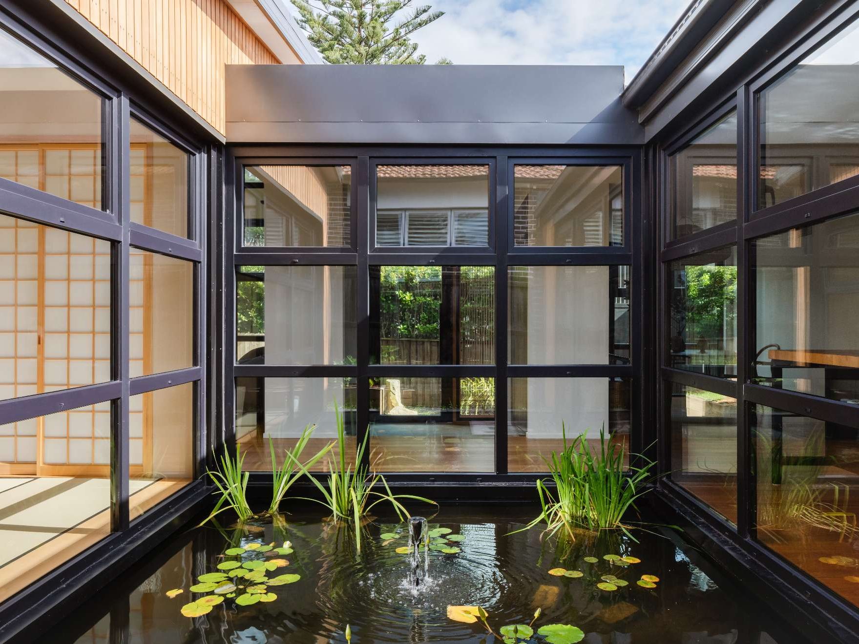 A tranquil courtyard reflection pond forms the serene heart of this home, framed by  black steel windows that invite nature into every room.
