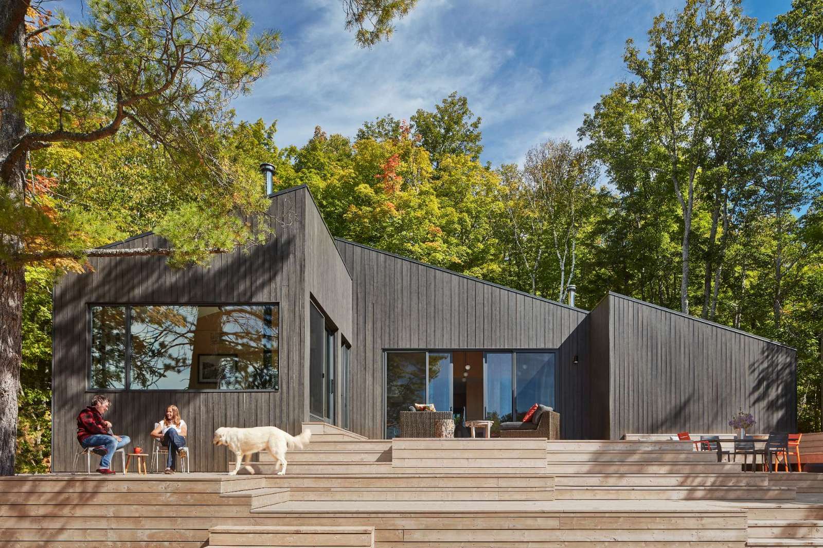 A modern one-storey cottage has three distinct volumes with integrated steep rooflines, and a large wood deck with multiple levels.