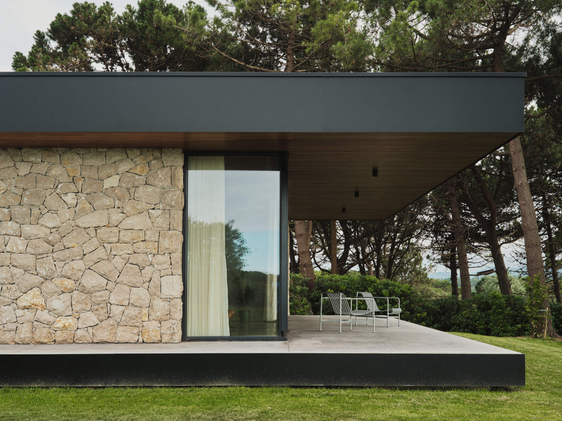 This modern home has limestone walls and large glass panels that form a rhythm of solid and void, while slatted wood ceilings, inside and out, accentuate the directional flow toward the sea.