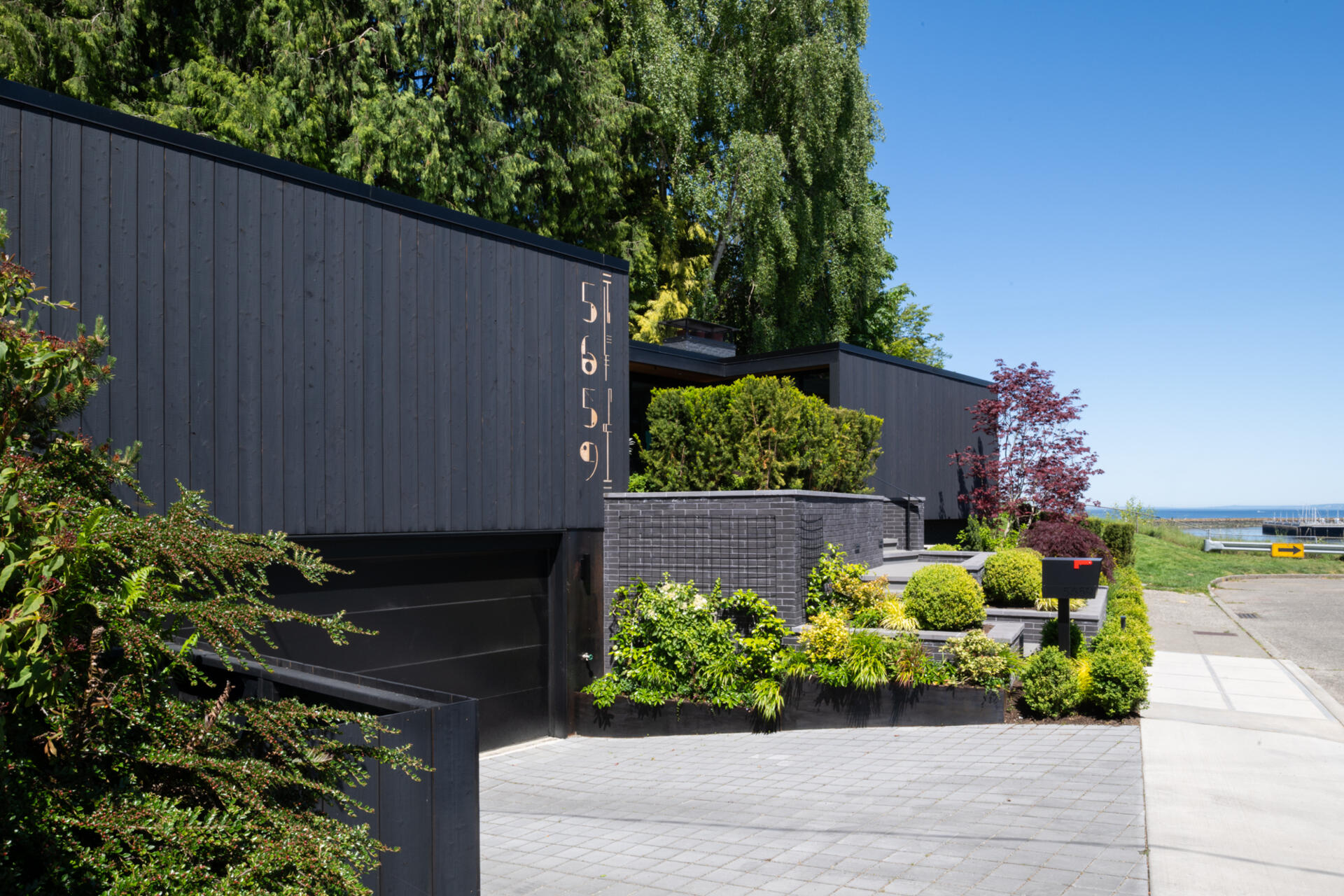 The bold shou sugi ban siding of this renovated mid-century modern home contrasts with the lush landscaping, while a pathway of stairs weaves through greenery to a welcoming patio.