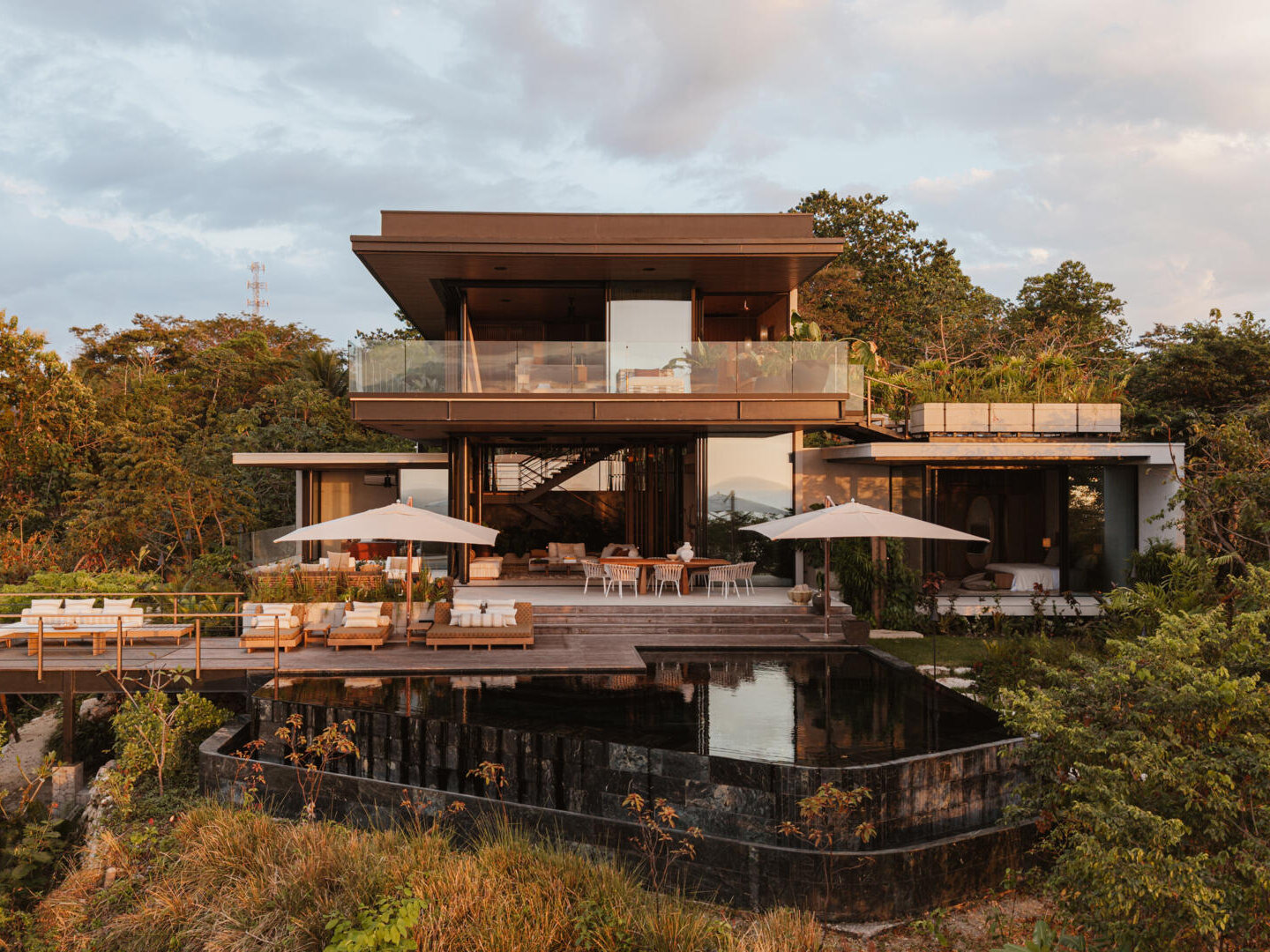 A modern house design with two pavilion-style volumes,  connected by a central vestibule, creates a layout that feels open, grounded, and deeply connected to the jungle canopy.
