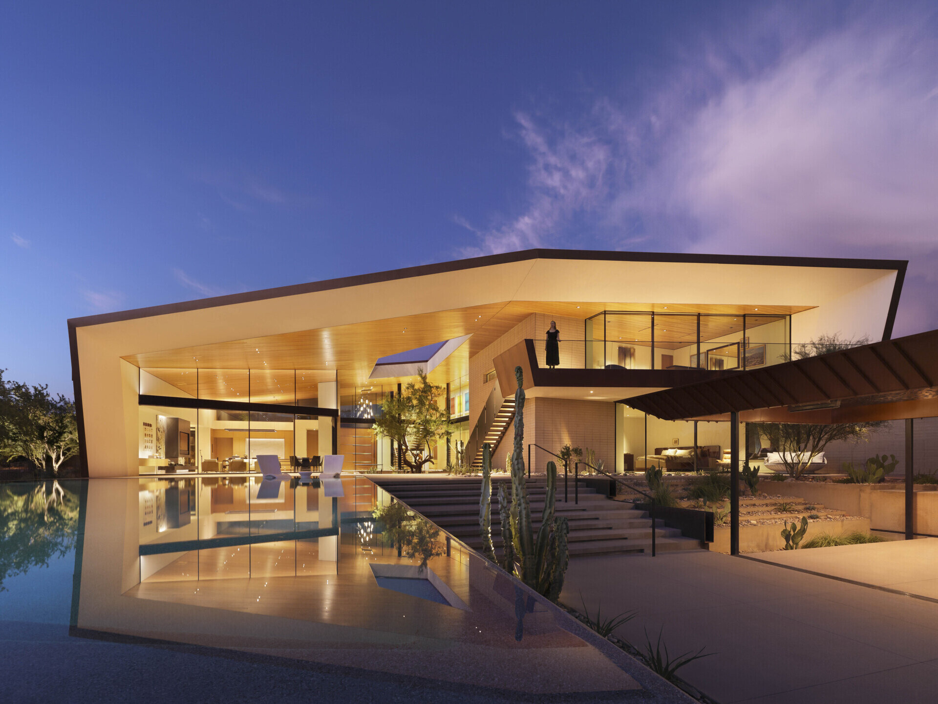 Defined by folding metal planes and rugged blasted-face masonry, the architecture of this modern house recalls the layered beauty of a geode. The weathered metal acts as a protective shell, sheltering the glass-filled interior that glows with natural daylight.