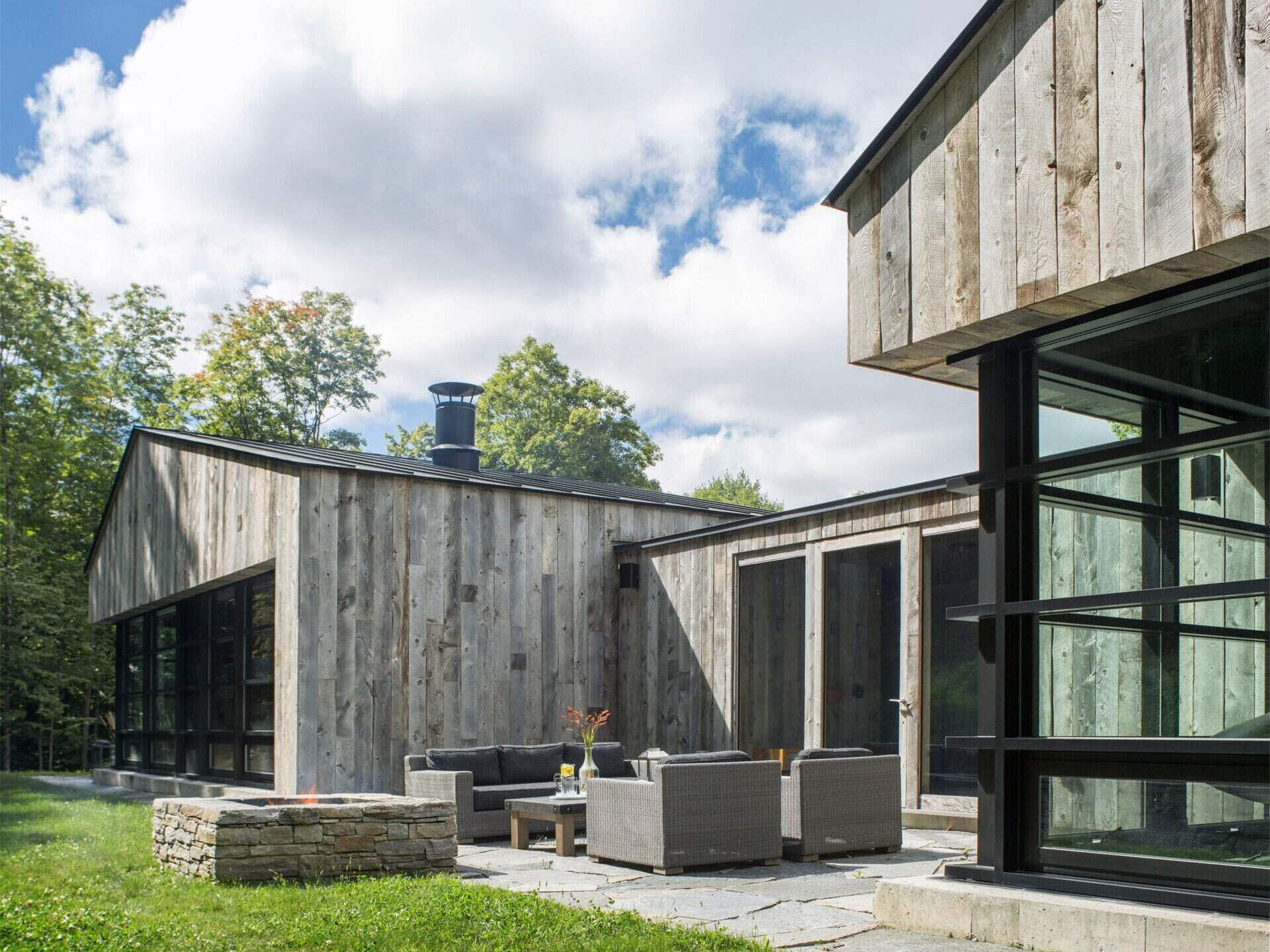 A Vermont guest house takes its shape from the classic woodshed, with gabled roofs that reimagine a familiar rural form. The house is clad in reclaimed snow fencing, weathered boards that give the structure instant character and texture.