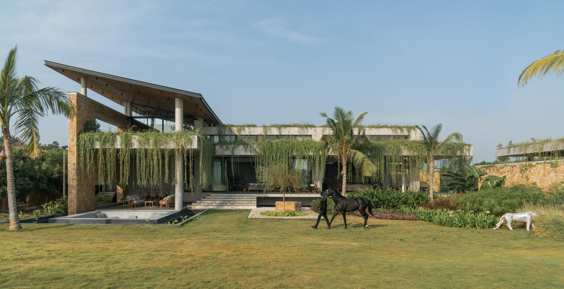 Long stone walls, floating pathways, and deep overhangs shape the architecture and guide movement through the home.